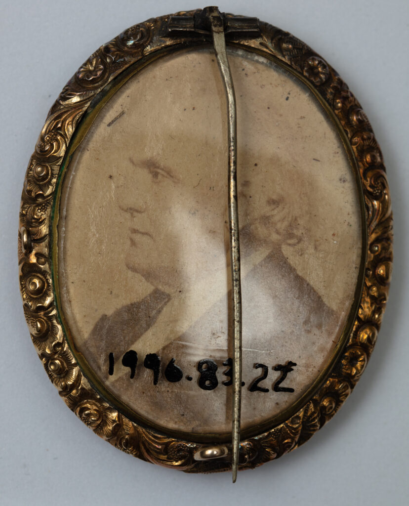 Verso of oval brooch featuring photograph of man in profile, bisected by pinback